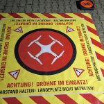 Faltbare Landefläche mit Warnaufdruck „Achtung! Drohne im Einsatz! Abstand halten!“ und vier Eckgewichten