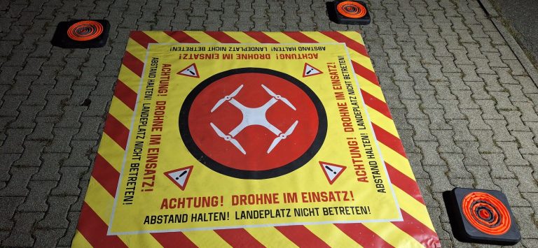 Faltbare Landefläche mit Warnaufdruck „Achtung! Drohne im Einsatz! Abstand halten!“ und vier Eckgewichten